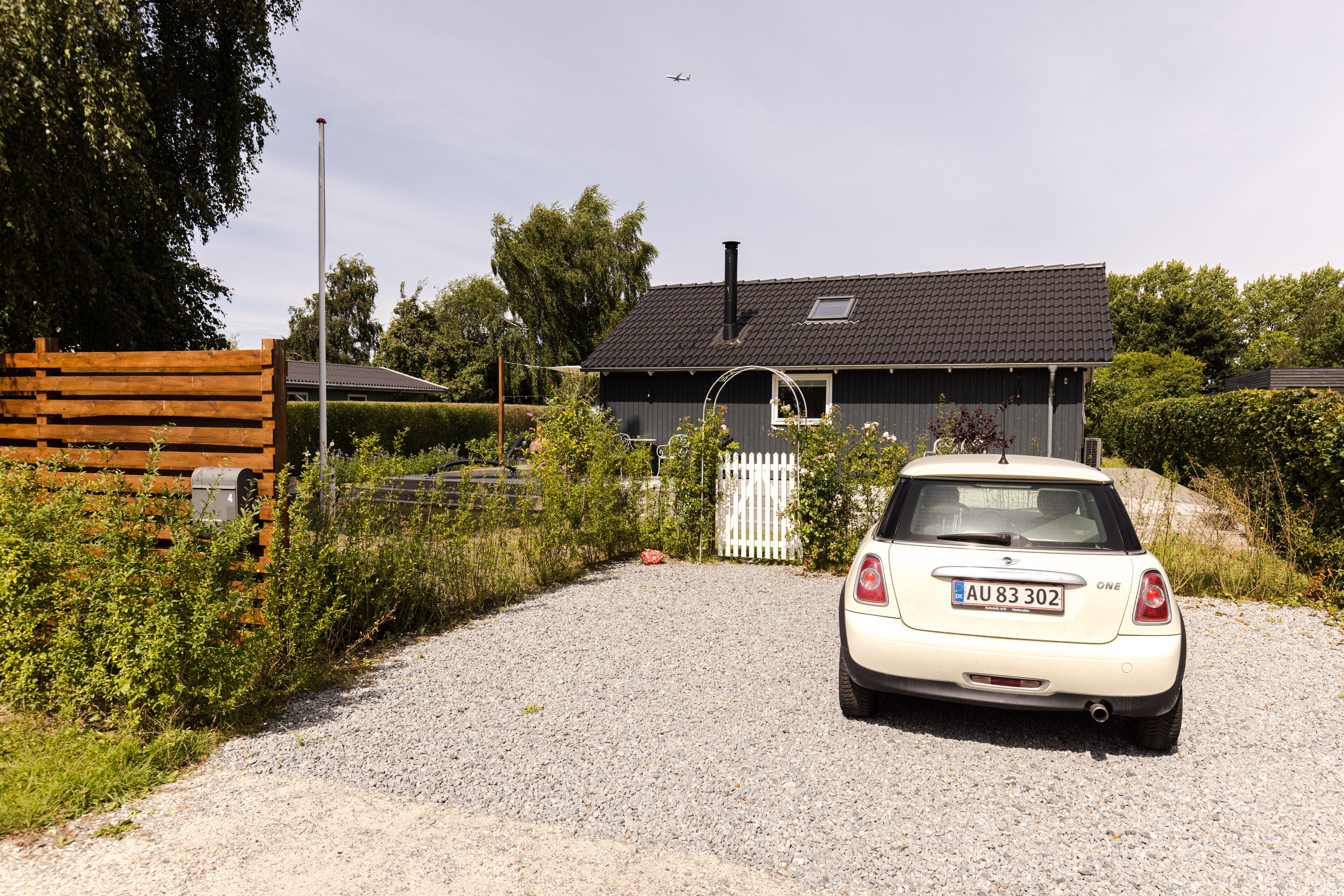 A white car parked in front of a house with a gravel driveway.