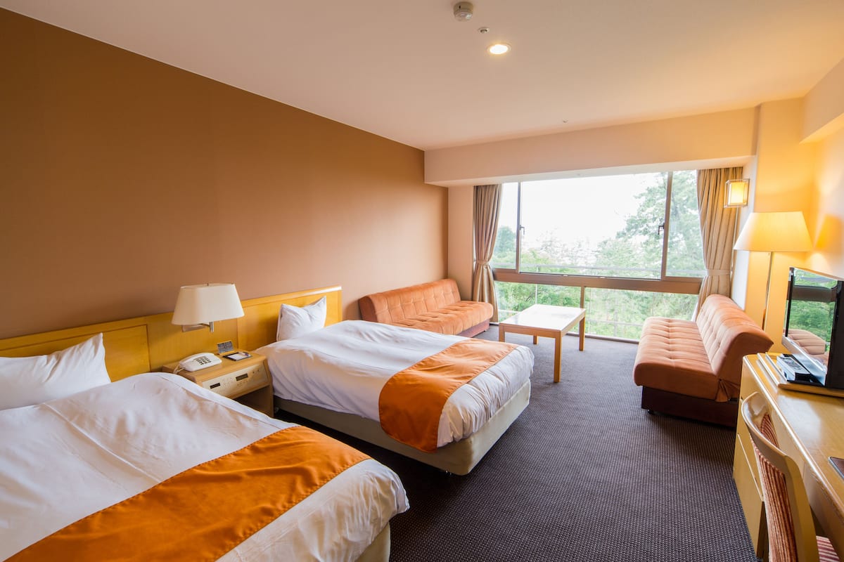 Una habitación de hotel con dos camas, un sofá, una mesita y un televisor.