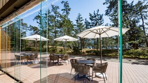 Un patio al aire libre con mesas y sillas, rodeado por paredes de vidrio y árboles.