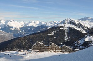 A large hotel with multiple floors and a ski resort in the background. - Charming 2 room apartment - view of Mont-Blanc - at the foot of the slopes in Aime 2000 (Plagne Aime 2000)