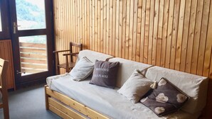 Una stanza con pavimento in legno, un divano letto, due lampade a parete e una porta che dà su un balcone.