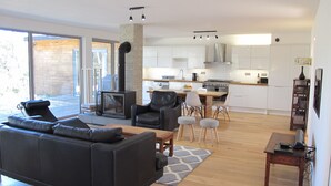 A modern living room with a black sofa, a fireplace, and a dining area with a wooden table and chairs. - Contemporary house with spectacular view of the forest (Notre-Dame-De-Monts)