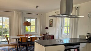 A modern kitchen with a central island, a dining area with a table and chairs, and a view of the outdoors through large windows. - Vacation apartment at Obstgut Willmann, quiet location with a view of Lake Constance (Kressbronn)