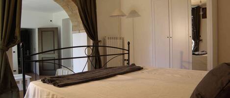 A bedroom with a bed, a mirror, a wardrobe, and an arched doorway.
