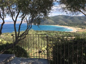 Un paysage côtier magnifique, avec un sentier menant à une plage, le tout entouré d’une végétation luxuriante et de collines.