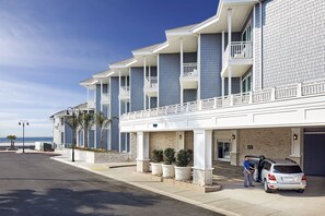 Un hotel con vistas al mar, que cuenta con una fila de balcones, un acceso cubierto y un estacionamiento.