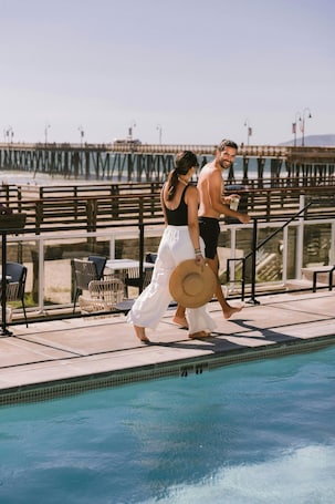 A poolside area with a view of a pier, outdoor seating, and a clear sky.