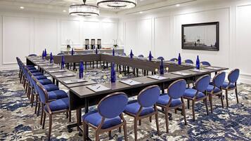 A conference room with a long table, blue chairs, and chandeliers.