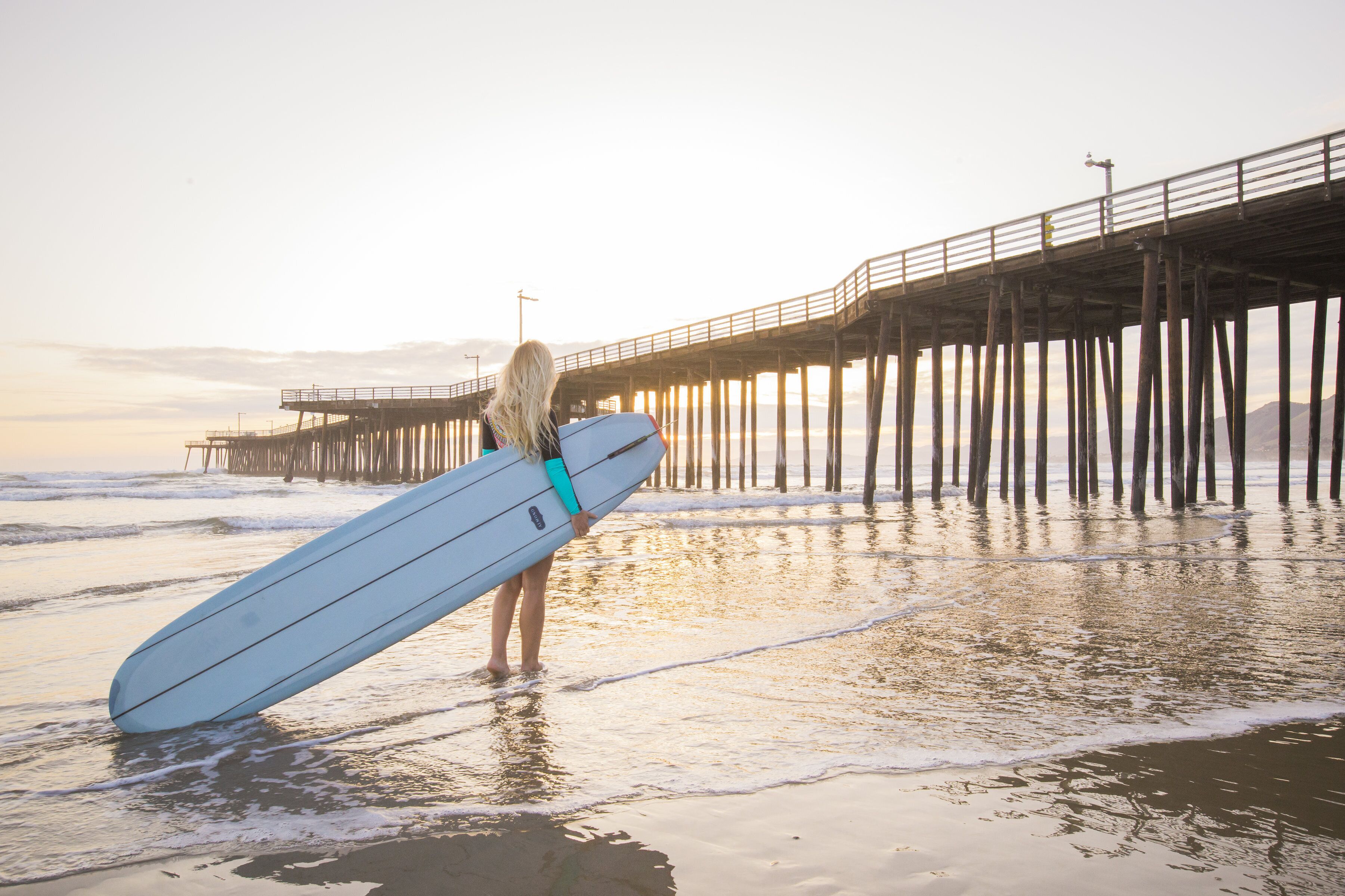 A pier extending into the water with a person holding a surfboard.