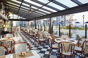 A covered outdoor seating area with checkered flooring, wicker chairs, and tables.