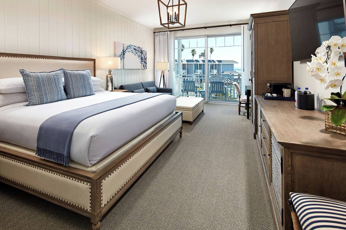 Une chambre d’hôtel avec un grand lit, un bureau avec un ordinateur, une chaise et un balcon avec des sièges d’extérieur.