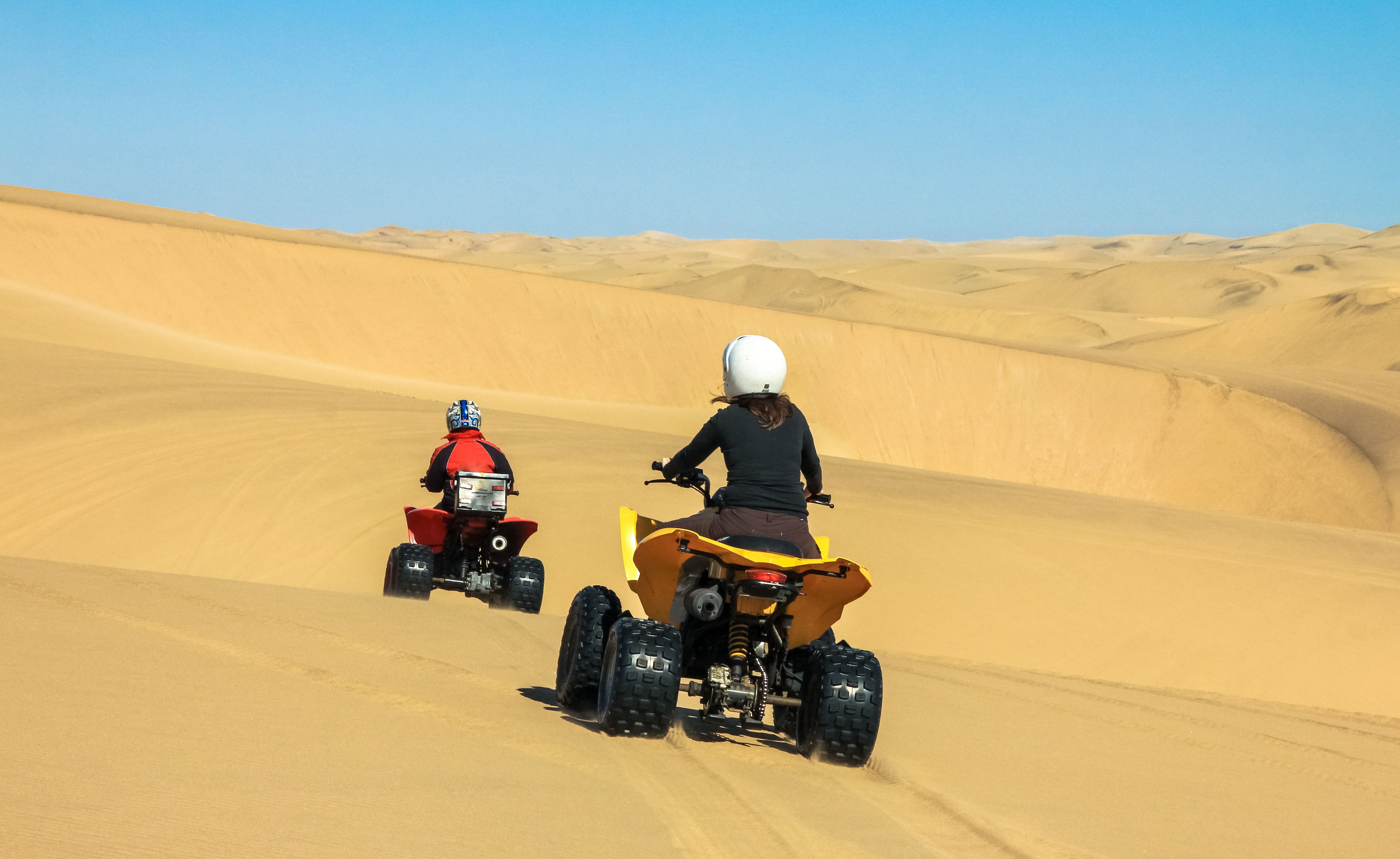 Two people riding quad bikes on a sandy dune.