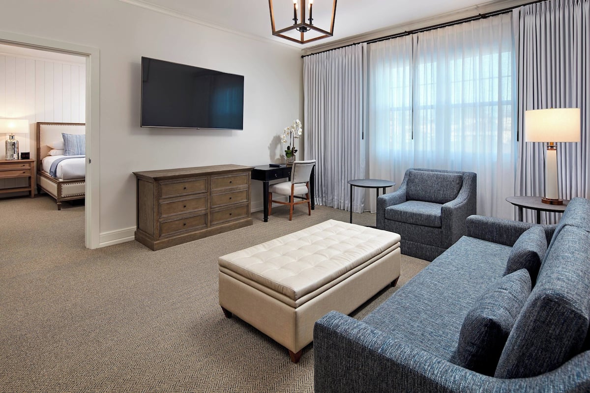 Une chambre d’hôtel comprenant un lit, un bureau, une chaise, un canapé, une télévision et une grande fenêtre avec des rideaux.