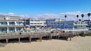 Ett hotell vid stranden med flera balkonger, ett poolområde och en strandpromenad av trä.