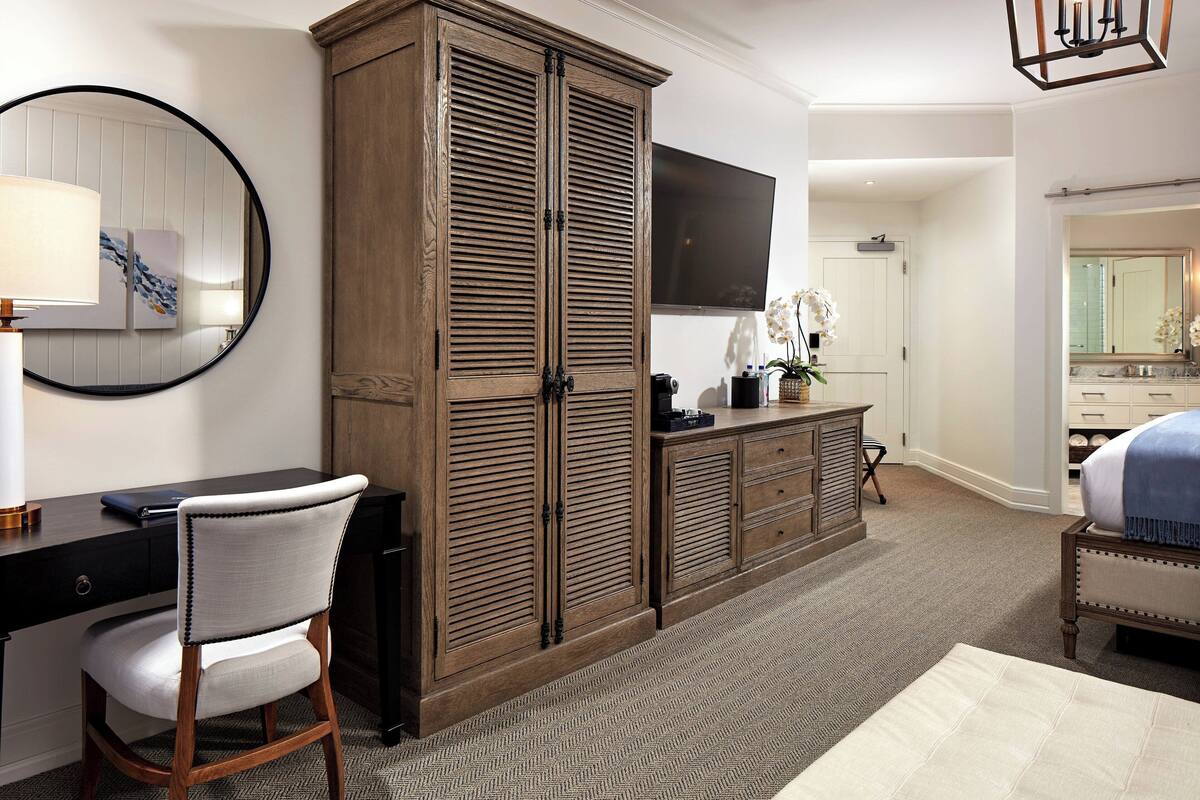 Une chambre avec une grande armoire, un bureau avec une chaise, une télévision et un lit.