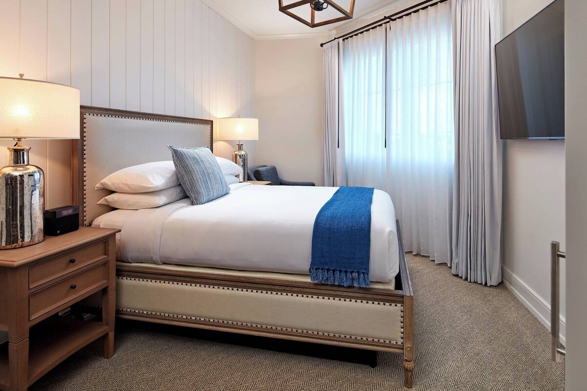 Une chambre d’hôtel avec un grand lit, deux tables de chevet, une télévision et une fenêtre avec des rideaux.