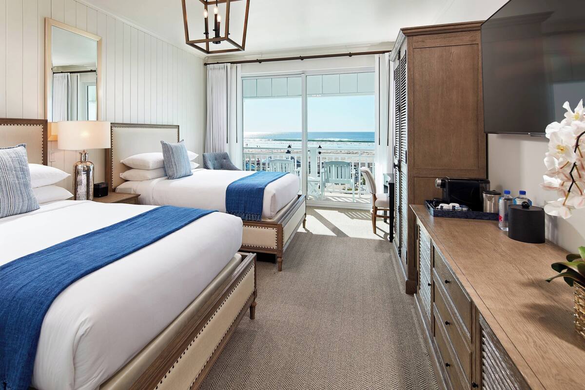 Une chambre d’hôtel avec deux lits, une grande télévision, un balcon avec vue sur l’océan et une commode en bois.