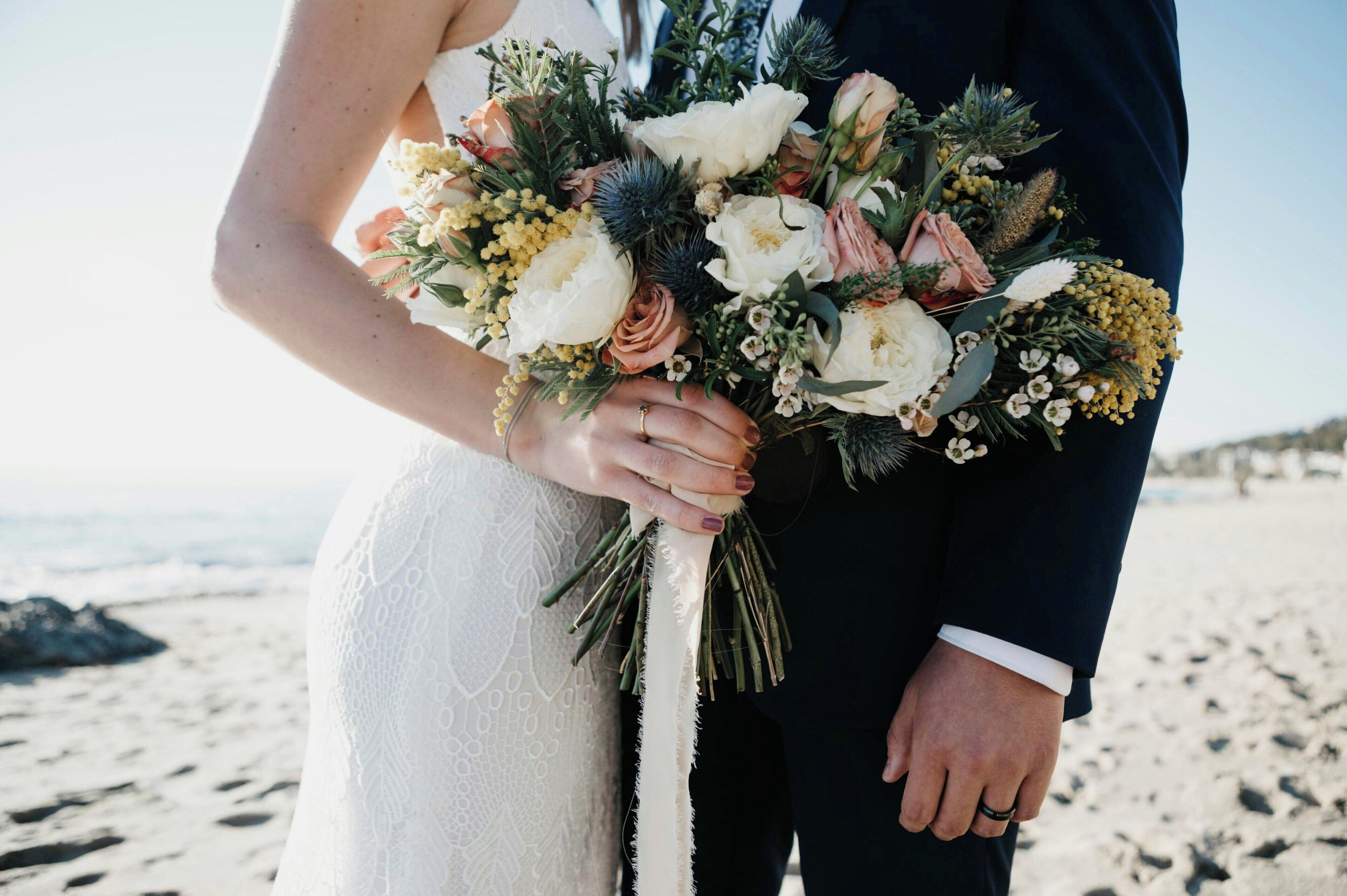 Un couple tenant un bouquet de fleurs sur une plage.