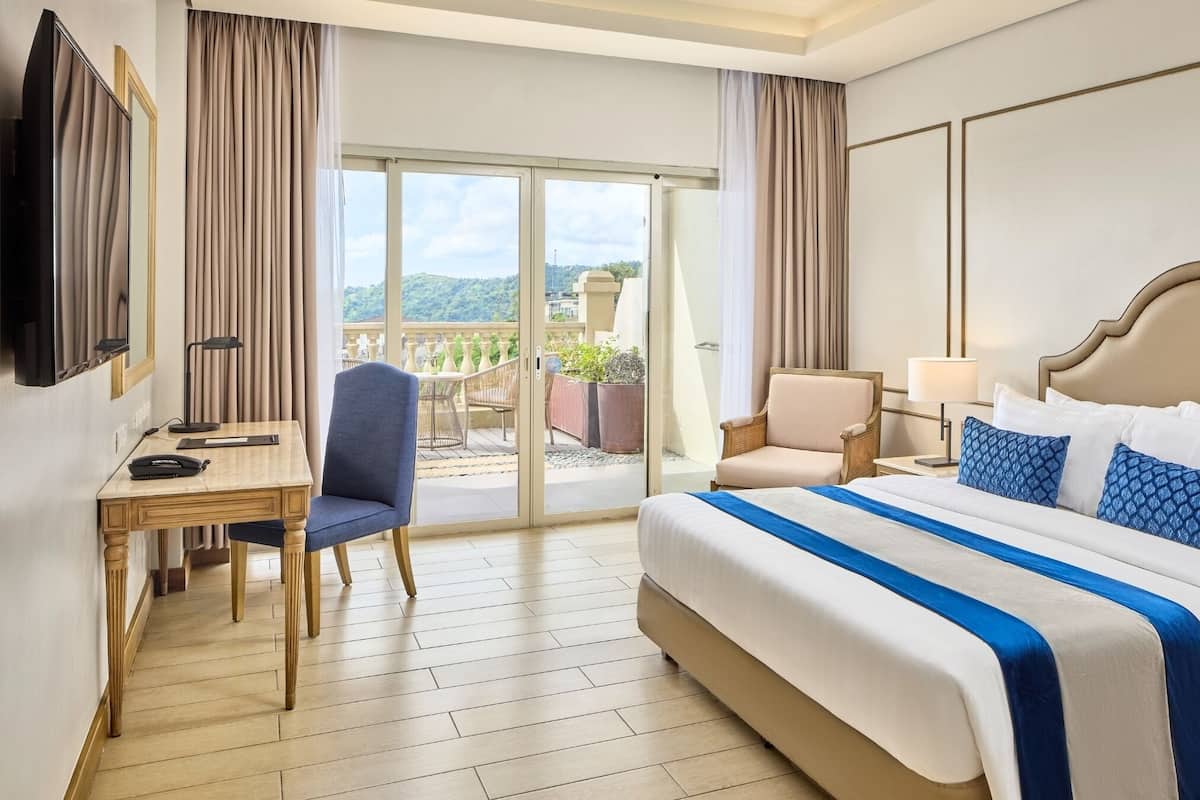 A hotel room with a bed, a desk, a chair, a TV, and a view of the outdoors.