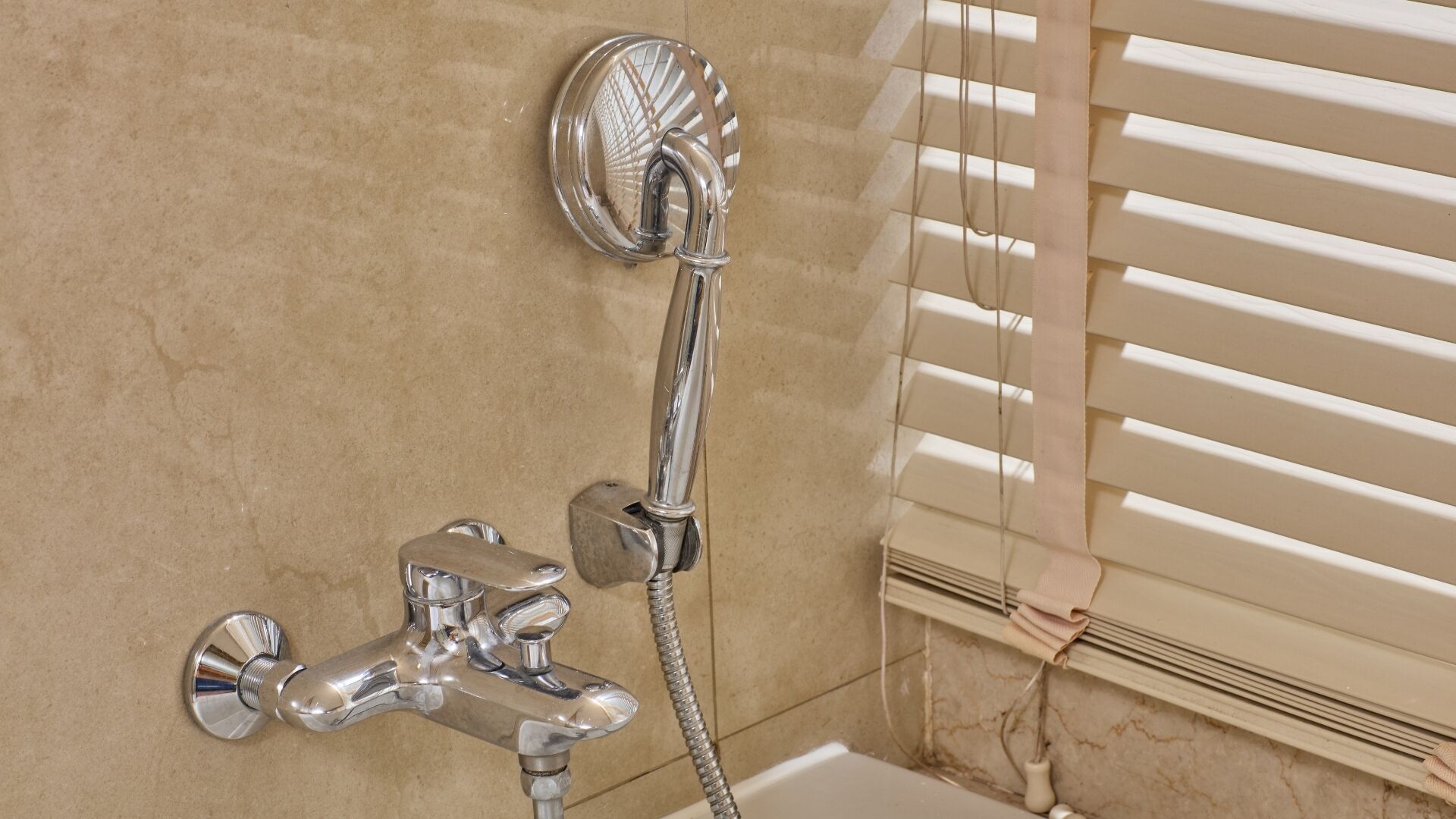Un baño con ducha, lavamanos y ventana con persianas.