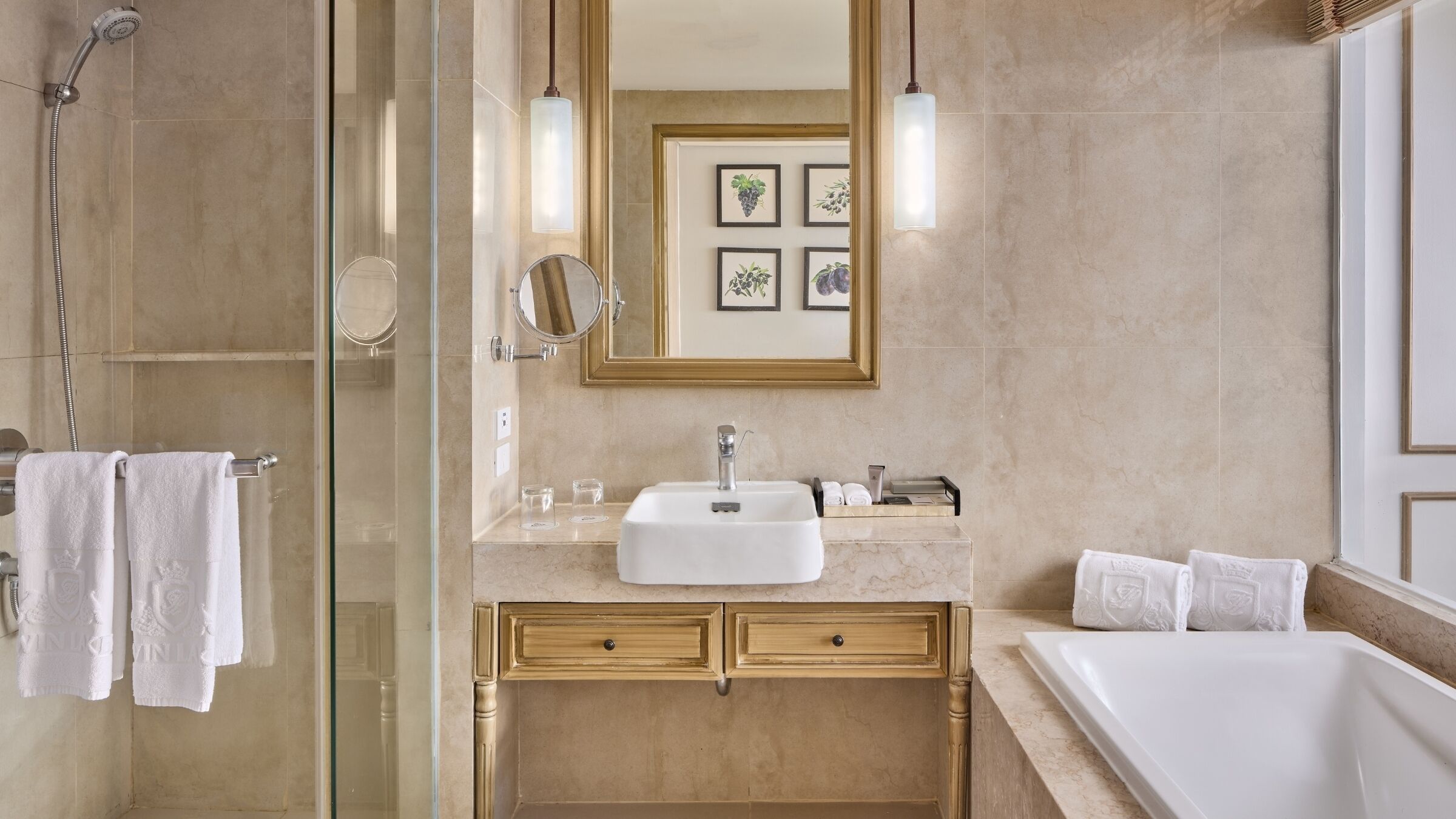A modern bathroom with a glass shower enclosure, a white sink, gold-toned cabinets, and a large bathtub.