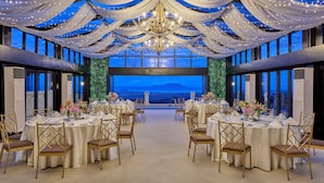 Un salón de banquetes con mesas redondas, sillas doradas y vista al mar.