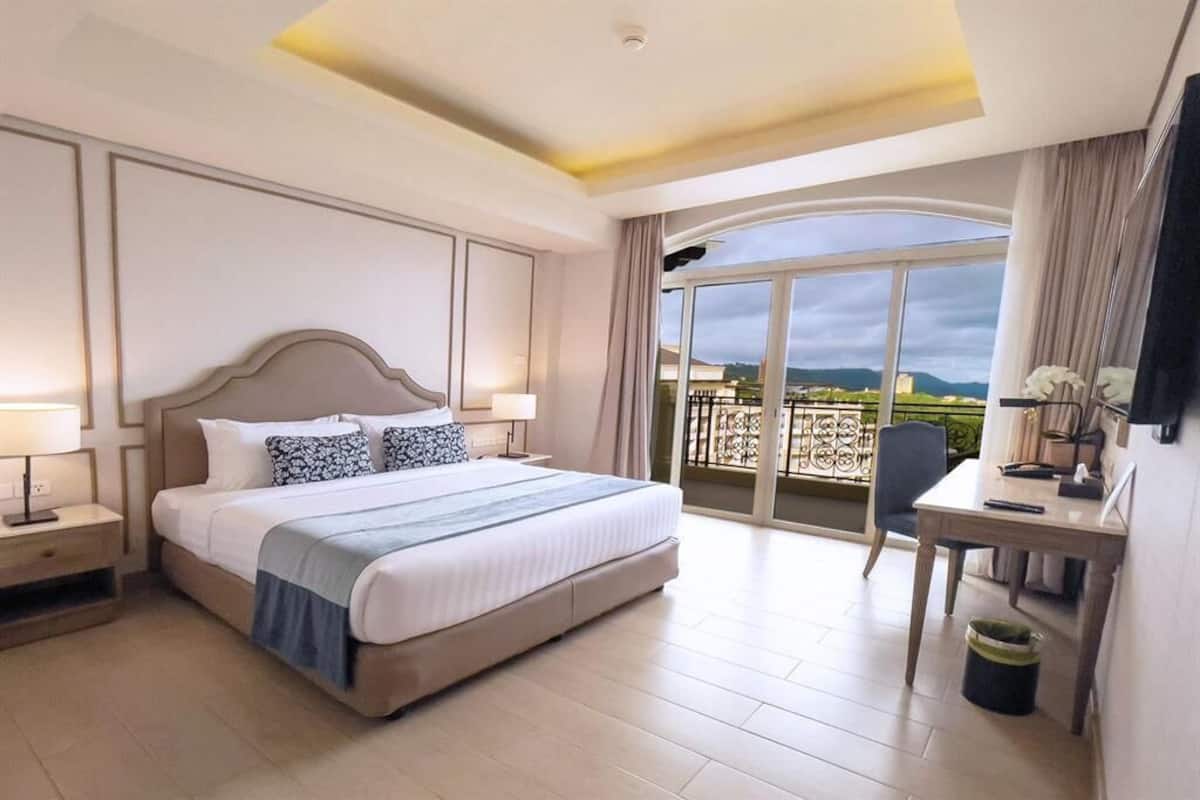 A hotel room with a large bed, a desk, and a balcony with a view.