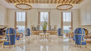 Un vestíbulo amplio con techos altos, candelabros y grandes ventanales que ofrecen vistas.
