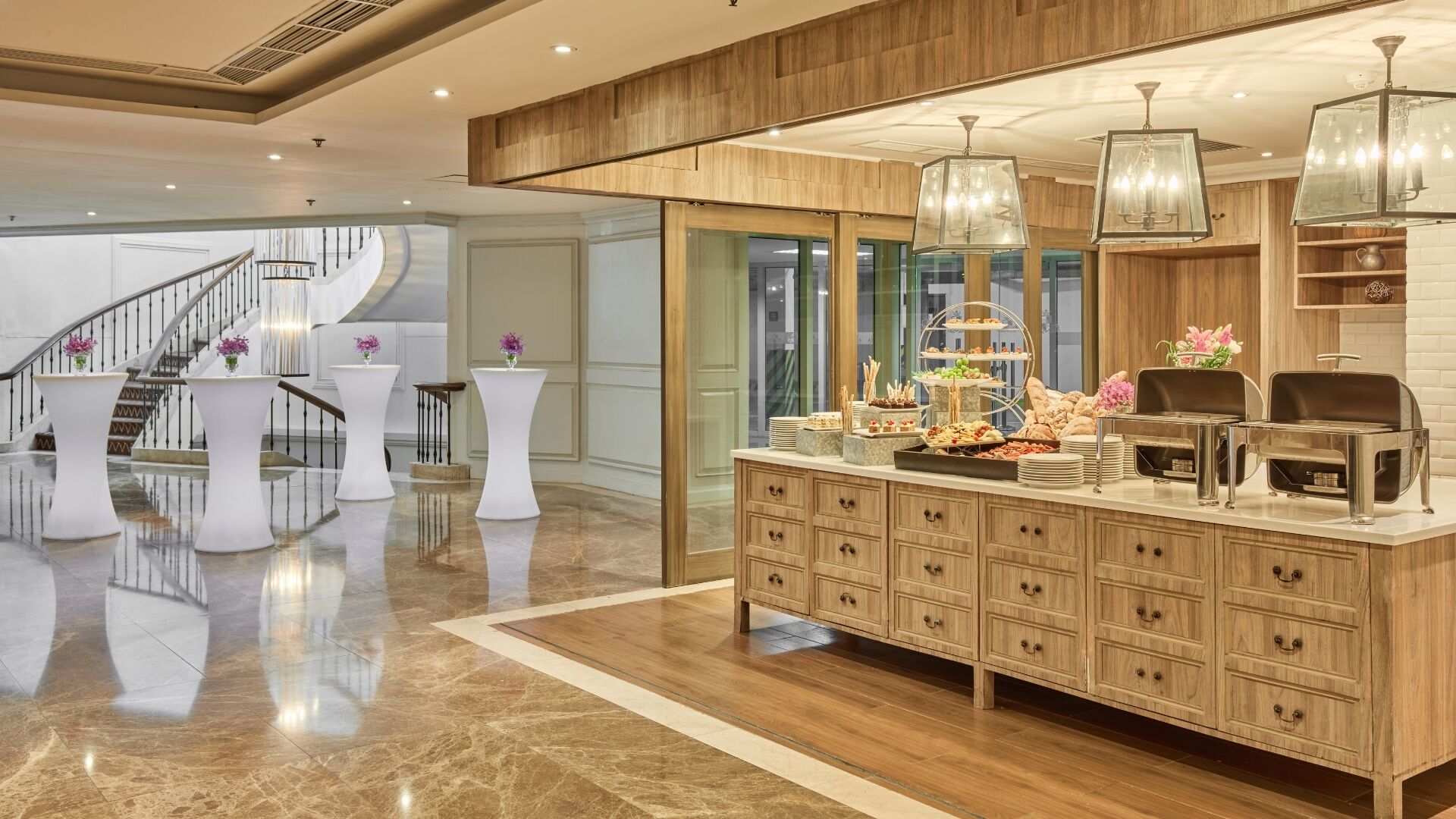 A modern hotel lobby with a marble floor, a wooden reception desk, and a staircase.