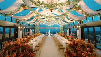 A banquet hall with a long table set for a wedding, decorated with flowers and draped fabric.