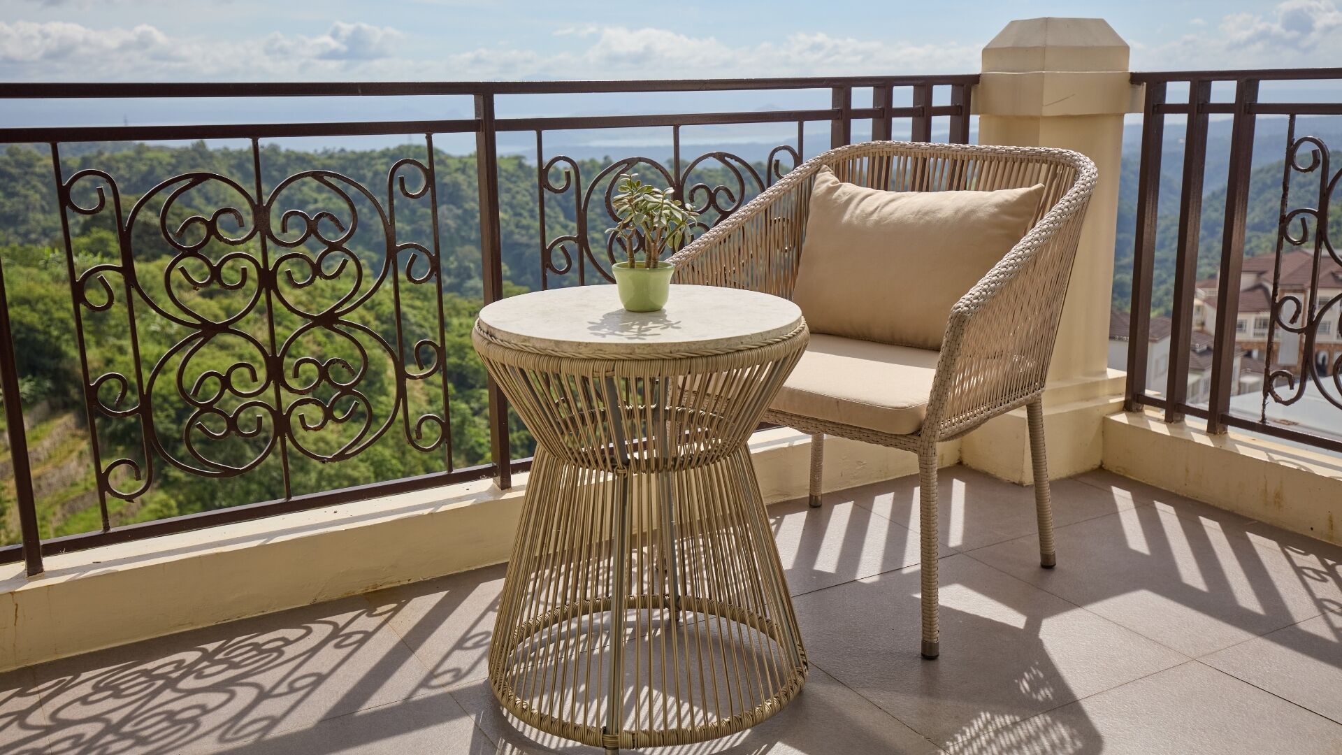 Un balcon avec une table et une chaise en osier, une plante en pot et une vue sur un paysage verdoyant.