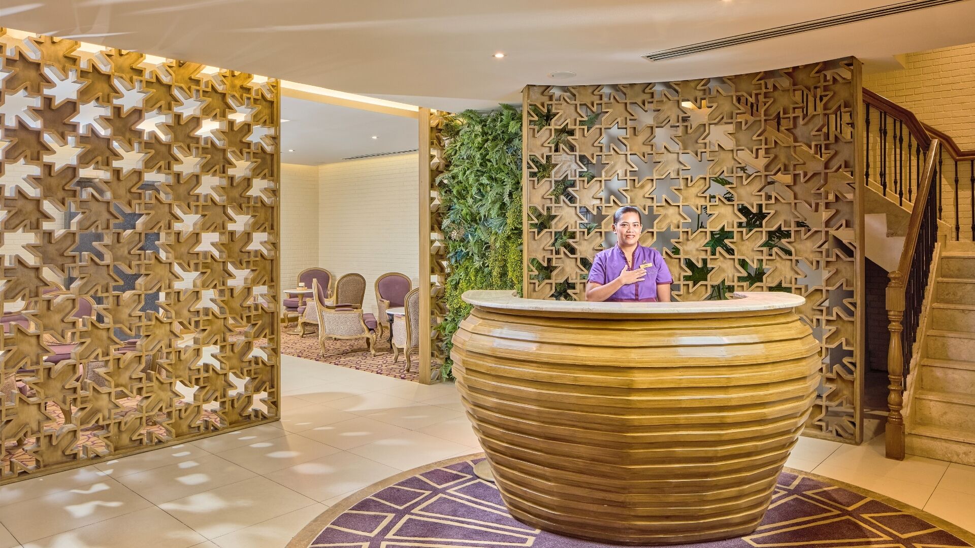 Zona de recepción con un amplio mostrador circular y texturizado, una recepcionista y una escalera a la derecha.