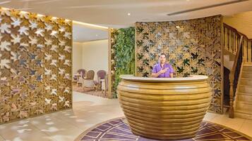 Zona de recepción con un amplio mostrador circular y texturizado, una recepcionista y una escalera a la derecha.