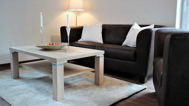 A living room with a wooden coffee table, a white candle, a lamp, and a brown leather sofa. - Apartment / Fitter Eal at the Thülsfelder dam (Friesoythe)