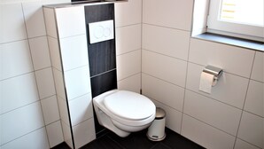 A compact, modern bathroom with a white toilet, a trash bin, and a window providing natural light. - Apartment / Fitter Eal at the Thülsfelder dam (Friesoythe)