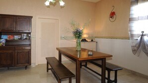A kitchen with a wooden table, bench, and a vase with flowers. There is a cabinet with items on the countertop and a wall with a decorative element.