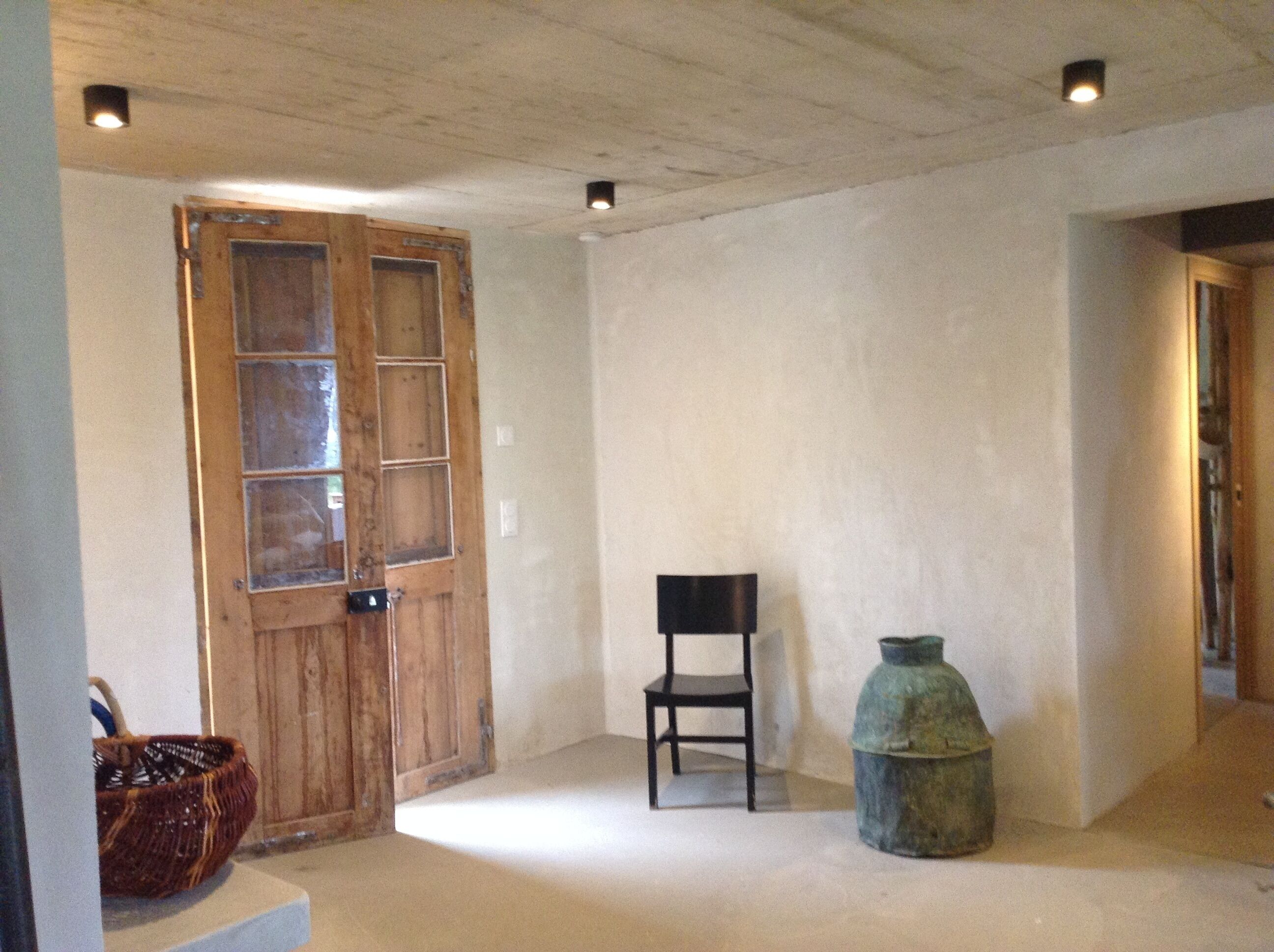 A room with a wooden door, a black chair, and a ceramic vase.