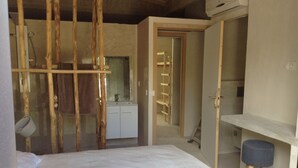 A bedroom with a bed, a wooden wardrobe, a small stool, and a bathroom visible through a doorway. - House Beachfront in Pinarello Bay. (Zonza)