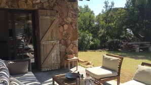A stone exterior wall, a wooden door, a wicker basket, a table with wine bottles and glasses, and outdoor seating with cushions. - House Beachfront in Pinarello Bay. (Zonza)