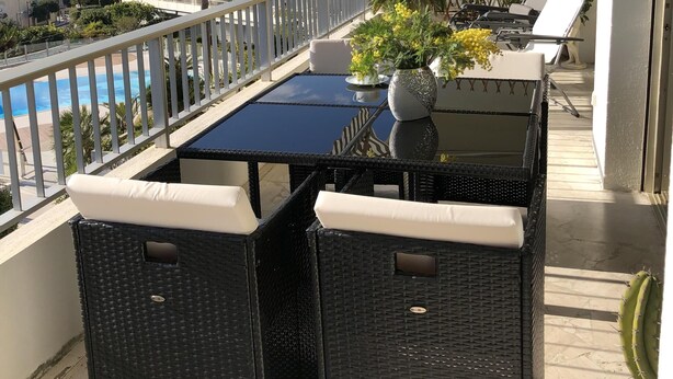 Een balkon met een tafel en stoelen, uitzicht op een zwembad en een berg op de achtergrond.