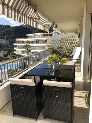 Un balcon avec une table et des chaises, une vue sur une piscine et une montagne en arrière-plan.