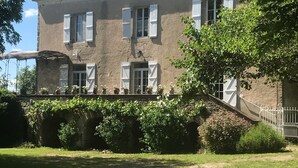 A large, two-story building with a stone facade, multiple windows with shutters, and a well-maintained garden area in front.