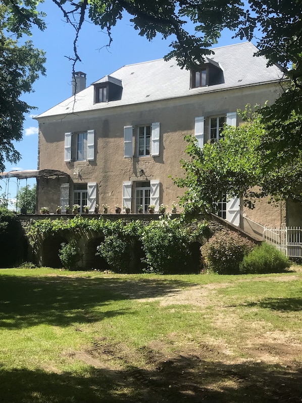 Un grand bâtiment à deux étages, doté d’une façade en pierre, de nombreuses fenêtres avec volets et d’un jardin bien entretenu à l’avant.