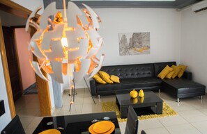 A modern living room with a black sofa, yellow cushions, a black coffee table, and a unique spherical light fixture.