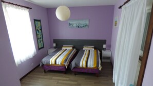 Una habitación con dos camas, piso de madera, ventilador de techo blanco y un cuadro en la pared.