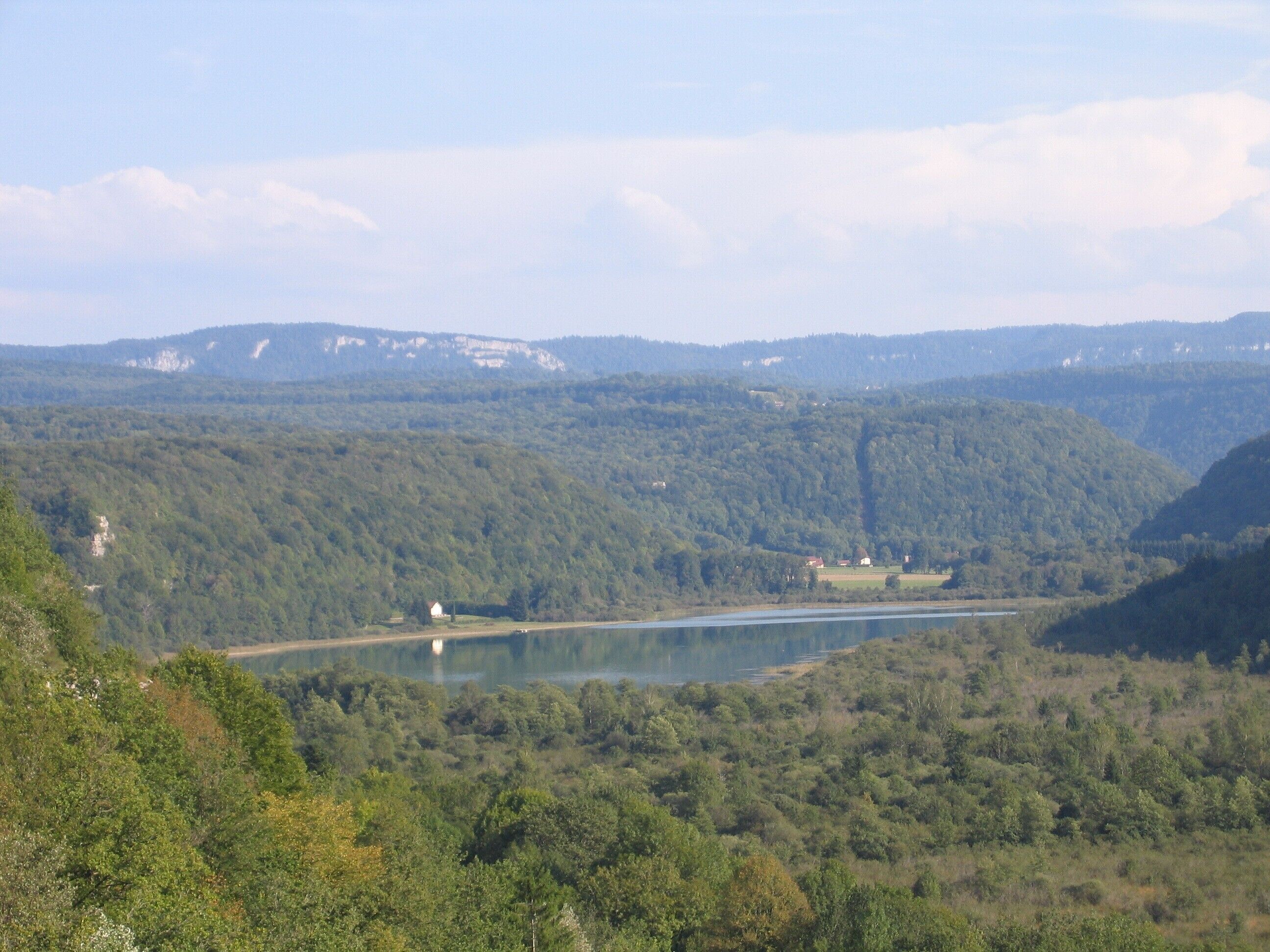 Un lac entouré de collines boisées, avec un petit bâtiment situé près du bord de l’eau.