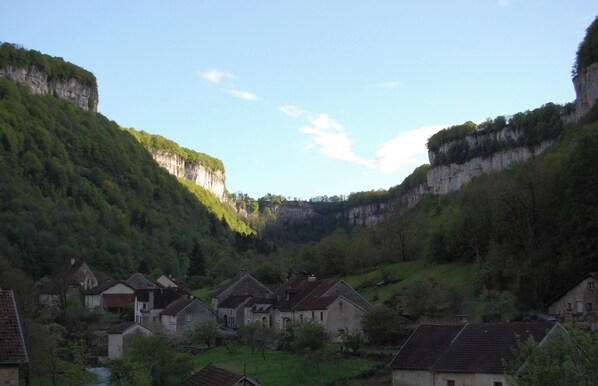 Un village aux bâtiments en pierre, traversé par une rivière et entouré de collines verdoyantes.