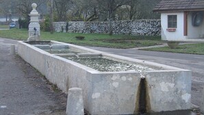 Una fuente rectangular central rodeada por un muro de piedra y un pequeño edificio con techo de tejas.