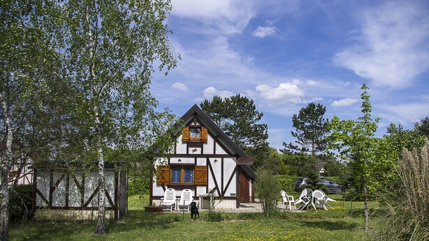 A traditional half-timbered house with a sloped roof, a small porch with chairs, and a fenced garden area. - Spring nature and sport in 'fleur de sologne' (Souvigny-En-Sologne)