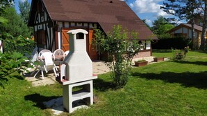 A traditional half-timbered house with a sloped roof, a stone chimney, and a small garden with a lawn and a few plants. - Spring nature and sport in 'fleur de sologne' (Souvigny-En-Sologne)